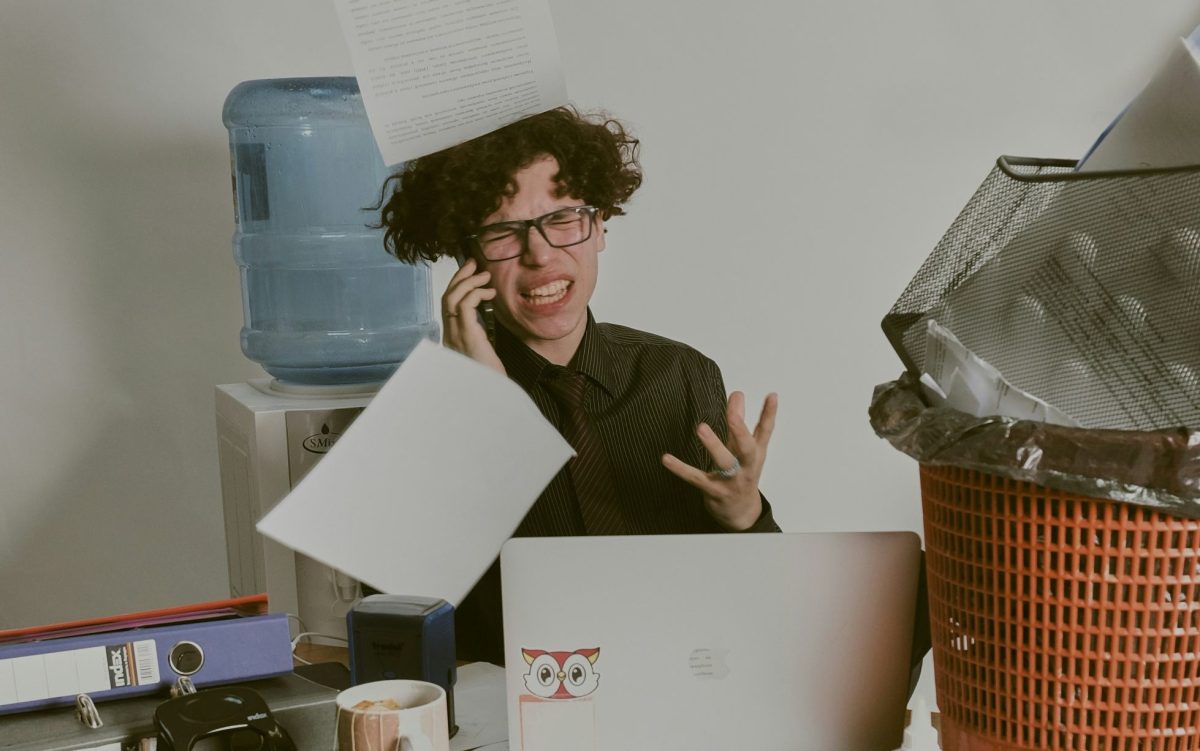 Literary agent. Image is a young Caucasian person on the phone sitting at a desk and throwing pages in the air in frustration.