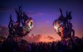Catch art and music at Suara Festival, Bali Indonesia. Two very large installations appear like masks hovering over a crowd with the sun setting into the background against a purple sky.
