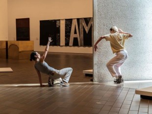 Two contemporary dancers make shapes with their bodies in a gallery setting.