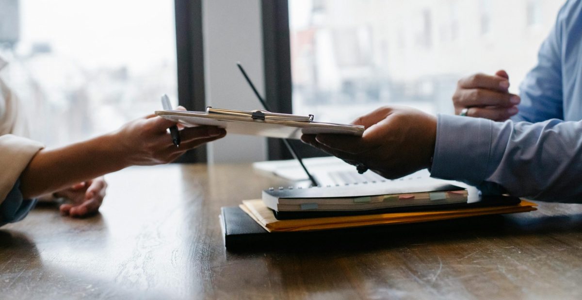 pay rise. Over a business desk one hand passes a clipboard to someone else's hand.