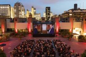 Barbican Centre, outdoor cinema 2024. A large crowd sitting in an open courtyard, watching a screen at night.