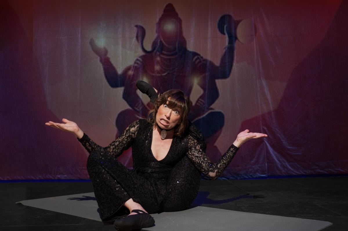 A woman in black is sprawled on the ground in a half seated position with her arms outstretched. Behind her is an image of a figure with multiple limbs. American Whore Story.