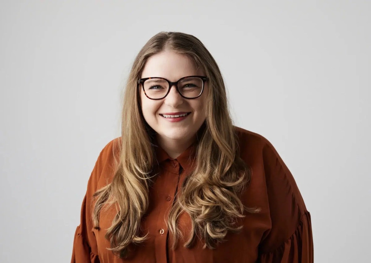 Woman with glasses and rust coloured shirt and auburn hair, smiling. Bec Melrose.