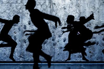 A group of dancers are seen in silhouette. There is a wall behind the covered with handprints. Giselle. Sadler's Wells Theatre.