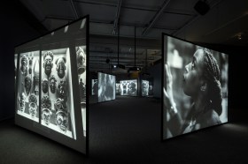 Multi screen video installation in black and white of woman looking at African objects. Isaac Julien.