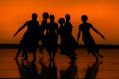 Silhouette of figures on stage with orange back lighting. Touring live theatre