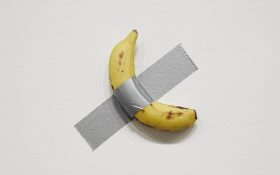 Installation view of Maurizio Cattelan's 'Comedian', 2019, on display in NGV Triennial 2023. A single banana duct-taped to a white wall.