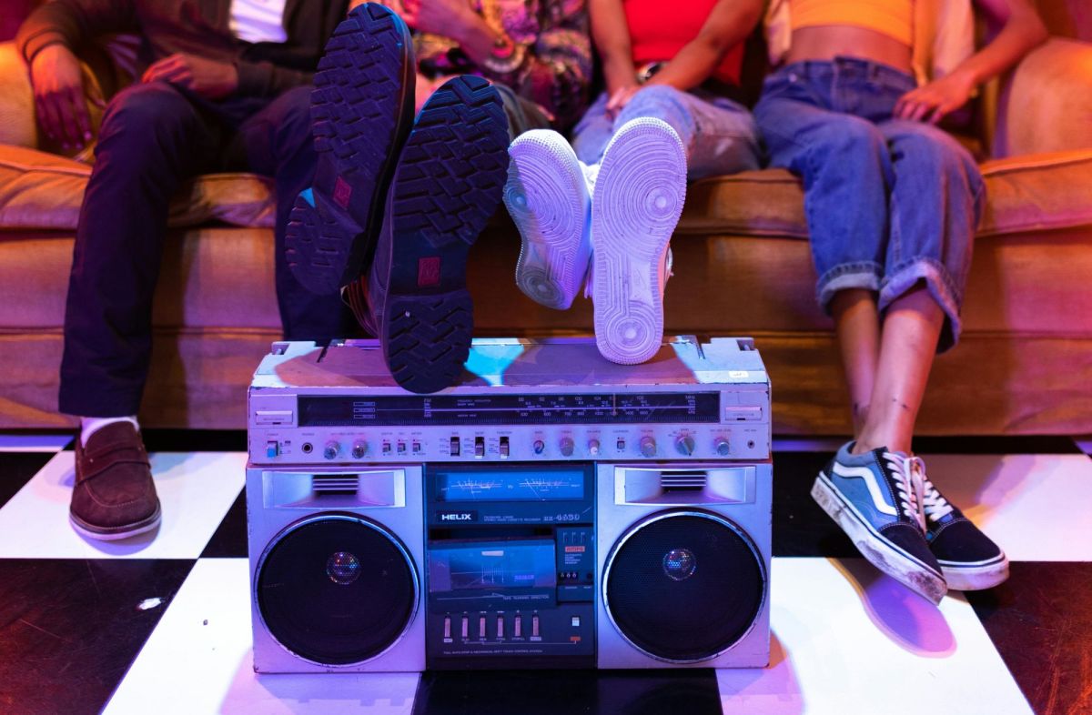 christmas music: colourful photo of three people's legs hanging off a loungeroom sofa, with an 1980s style ghettoblaster stereo on the floor in front of their feet.