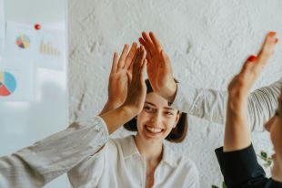 arts managers, best workers: A young white woman smiling while "high fiving" a group of three other people.