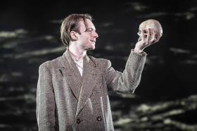 A young man in a tweed suit holding up a skull.